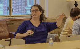 Stephanie Lanza, a white woman with glasses and brown hair in a blue sweater, talks to the group.