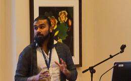 Mohanraj Krishnan, a faculty member wearing a long cardigan and white button-up, presents to the group.
