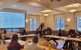 Mohanraj Krishnan, a faculty member wearing a long cardigan and white button-up, presents to the group in a wide shot.