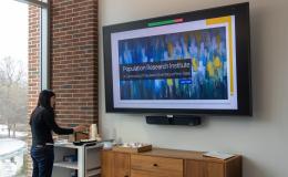 A woman wearing all black helps herself to some refreshments next to a large TV screen.