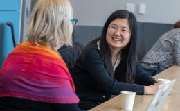 Two women, one dressed in black and another with a multicolored scarf, speak to each other.