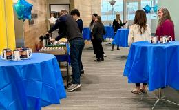 Attendees gathered around tables with blue tablecloths on them in the new Susan Welch Liberal Arts Building.