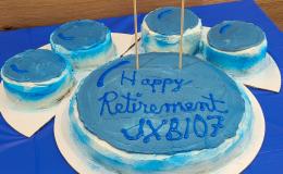 Pawprint shaped cake with blue and white frosting that says 'Happy Retirement JXB107."