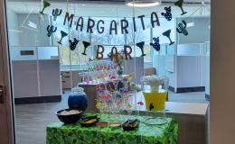 Green tablecloth covered table with a drinks station and a banner that says "Margarita Bar" on it.