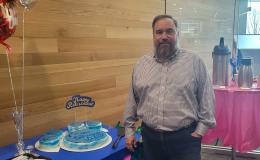 Joe Broniszewski, a middle-aged white man standing next to his retirement cake.