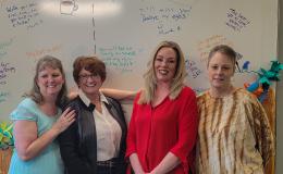Group shot of four white women posed in front of a white board.