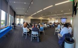 Wideshot of the conference attendees sitting down at round tables.