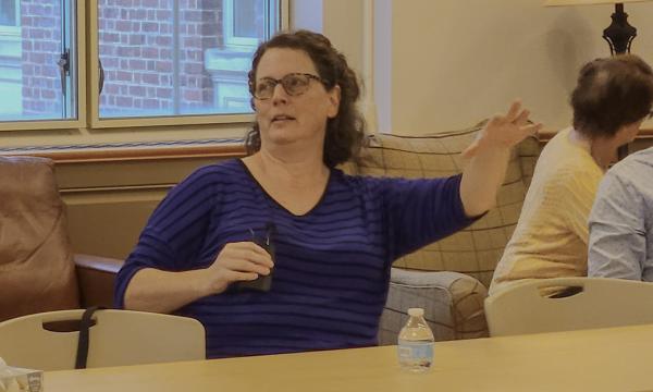 Stephanie Lanza, a white woman with glasses and brown hair in a blue sweater, talks to the group.