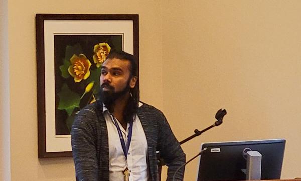 Mohanraj Krishnan, a faculty member wearing a long cardigan and white button-up, presents to the group.