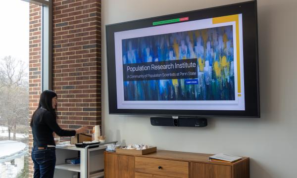 A woman wearing all black helps herself to some refreshments next to a large TV screen.